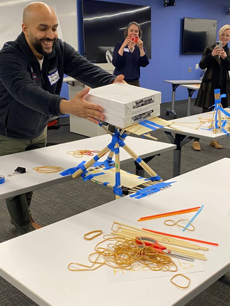 a student using two stacks of copy paper to test if their building project can successfully bear weight.