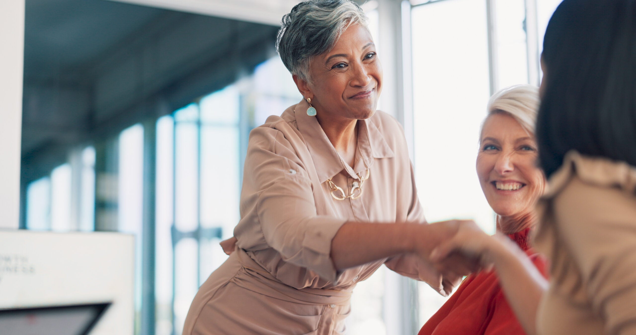 A businesswoman shaking the hand of another businesswoman in a conference room.