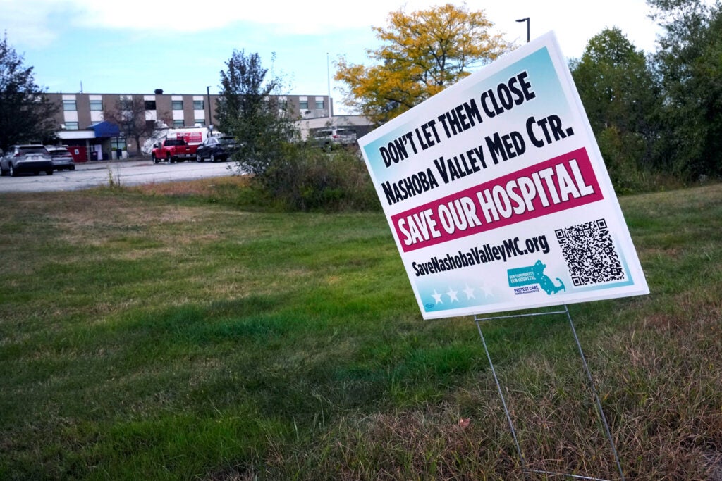 A white and magenta yard sign reads "Save our hospital" 