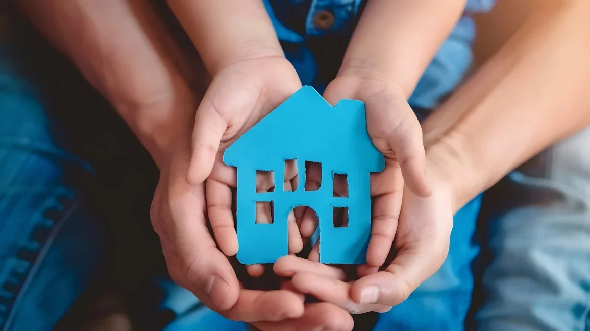 Close-up of adult and child hands holding a blue clay cut-out of a house