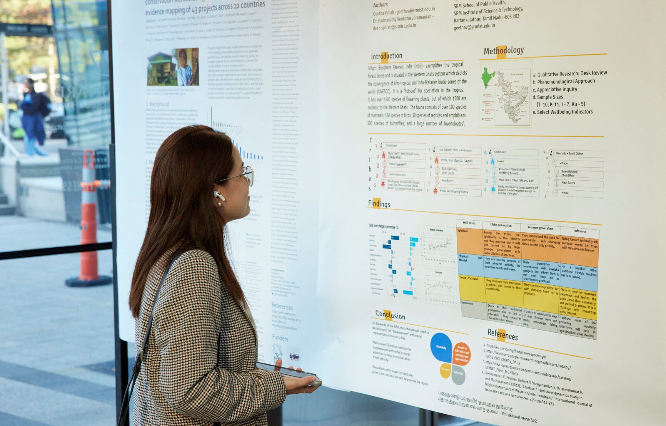 A student with long hair and a tweed jacket reading a research poster