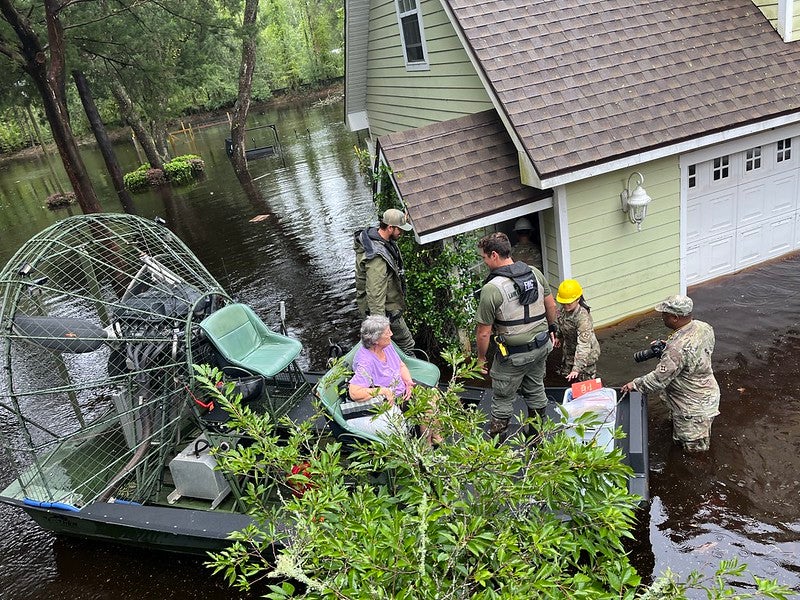 FWC and Florida State Guard officers assist resident out of a flooded home by way of airboat.