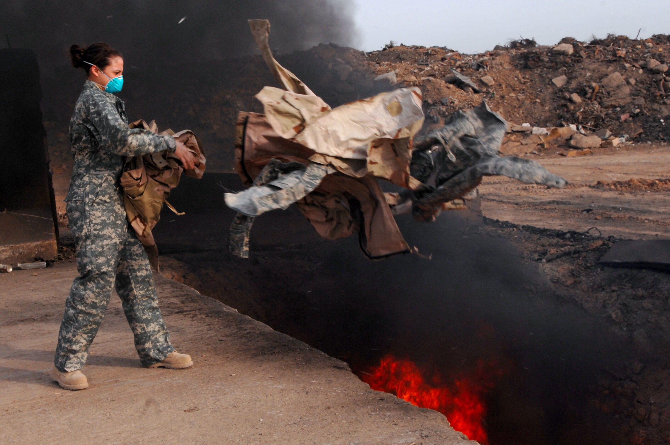 Senior Airman Frances Gavalis, 332nd Expeditionary Logistics Readiness Squadron equipment manager, tosses unserviceable uniform items into a burn pit, March 10. Military uniform items turned in must be burned to ensure they cannot be used by opposing forces. Airman Gavalis is deployed from Kirtland Air Force Base, N.M. (U.S. Air Force photo/Senior Airman Julianne Showalter)