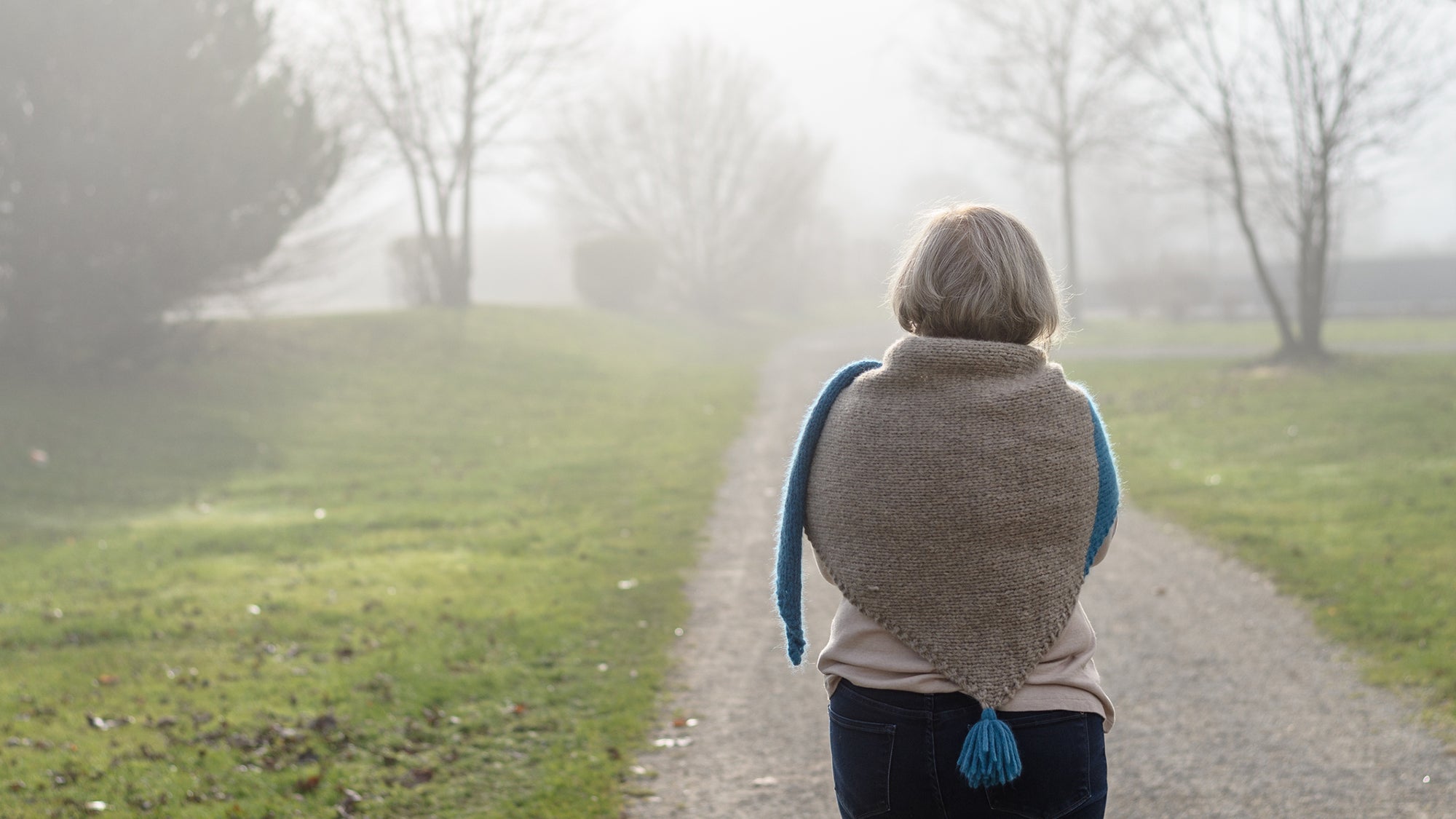 older woman pictured from behind, walking on a path