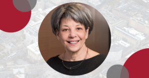 Headshot of Cindy Mann, Former Director of Medicaid for Centers for Medicare and Medicaid Services CMS. In the background, there is a faint image of the Boston skyline with circle designs.