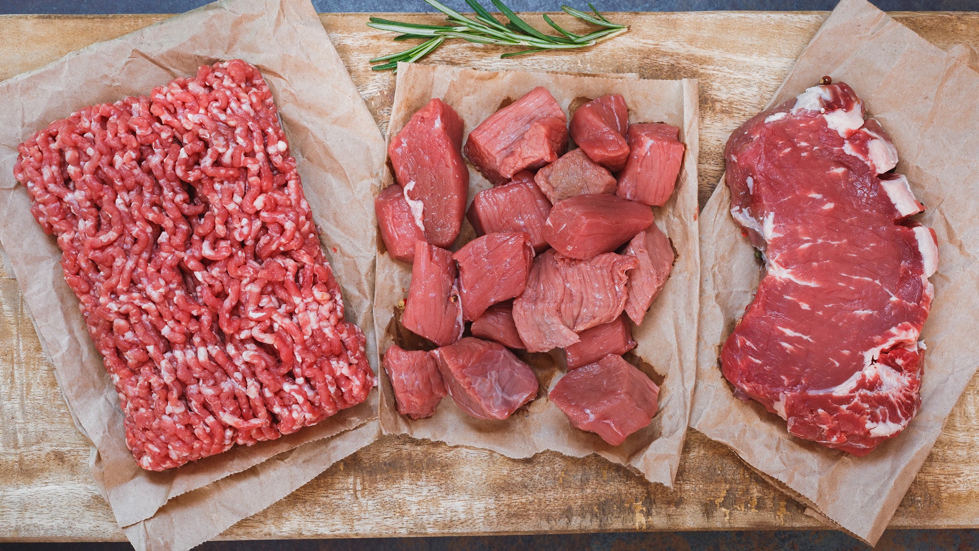 Three kinds of raw red meat, including chopped meat, stew meat, and steak, on parchment paper, top view