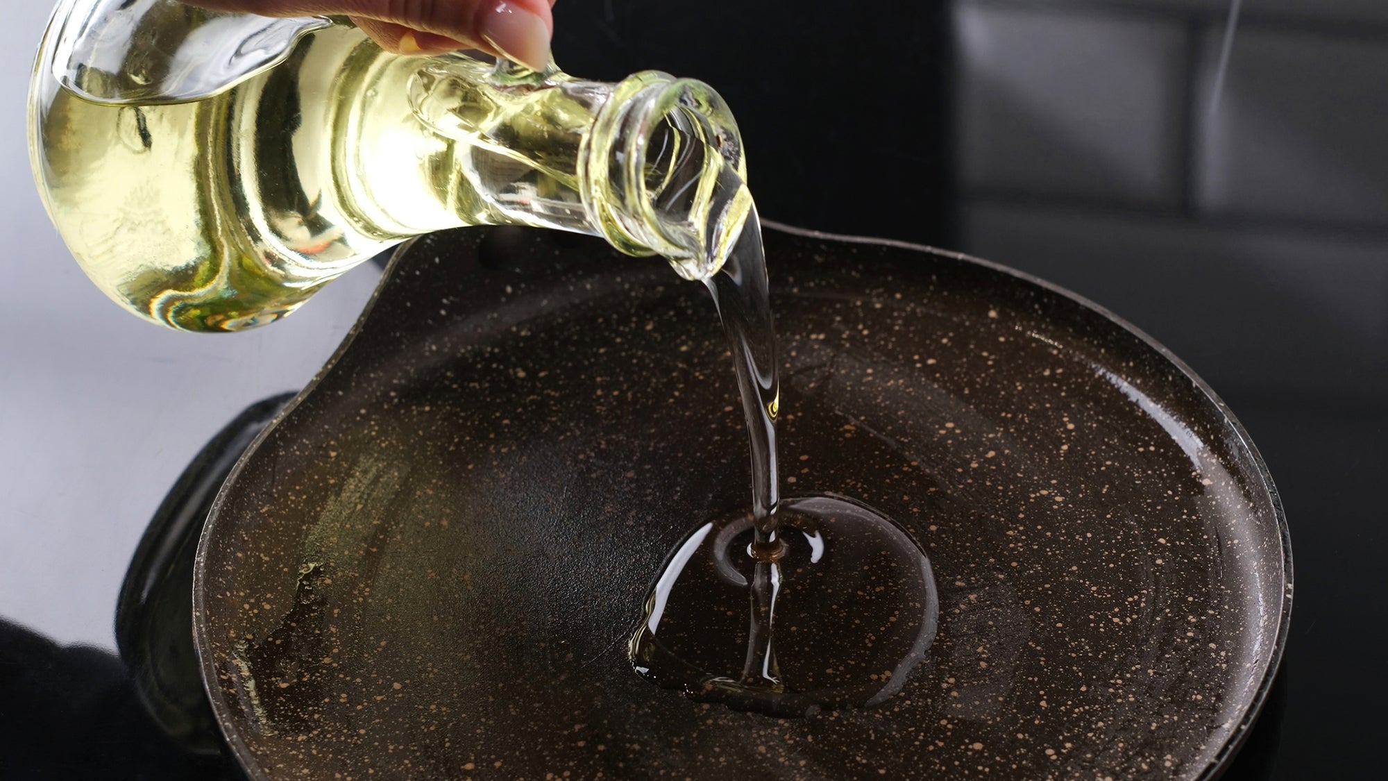 A person pours oil onto a hot cooking pan.