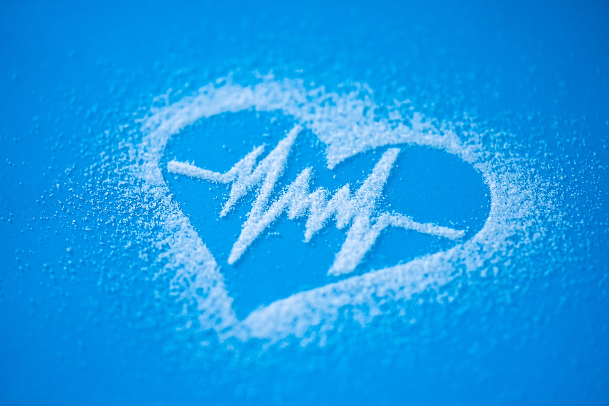 Grains of salt arranged into the shape of a heart with a heart beat line inside, on a bright blue background.