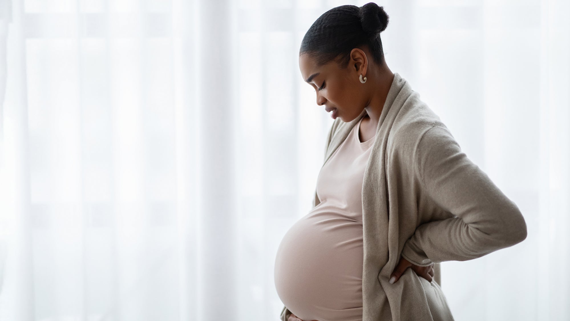 A Black pregnant woman standing by a window