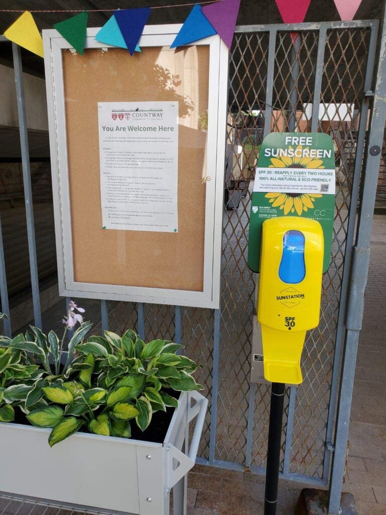 A yellow sunscreen station stands on the pavement outside.