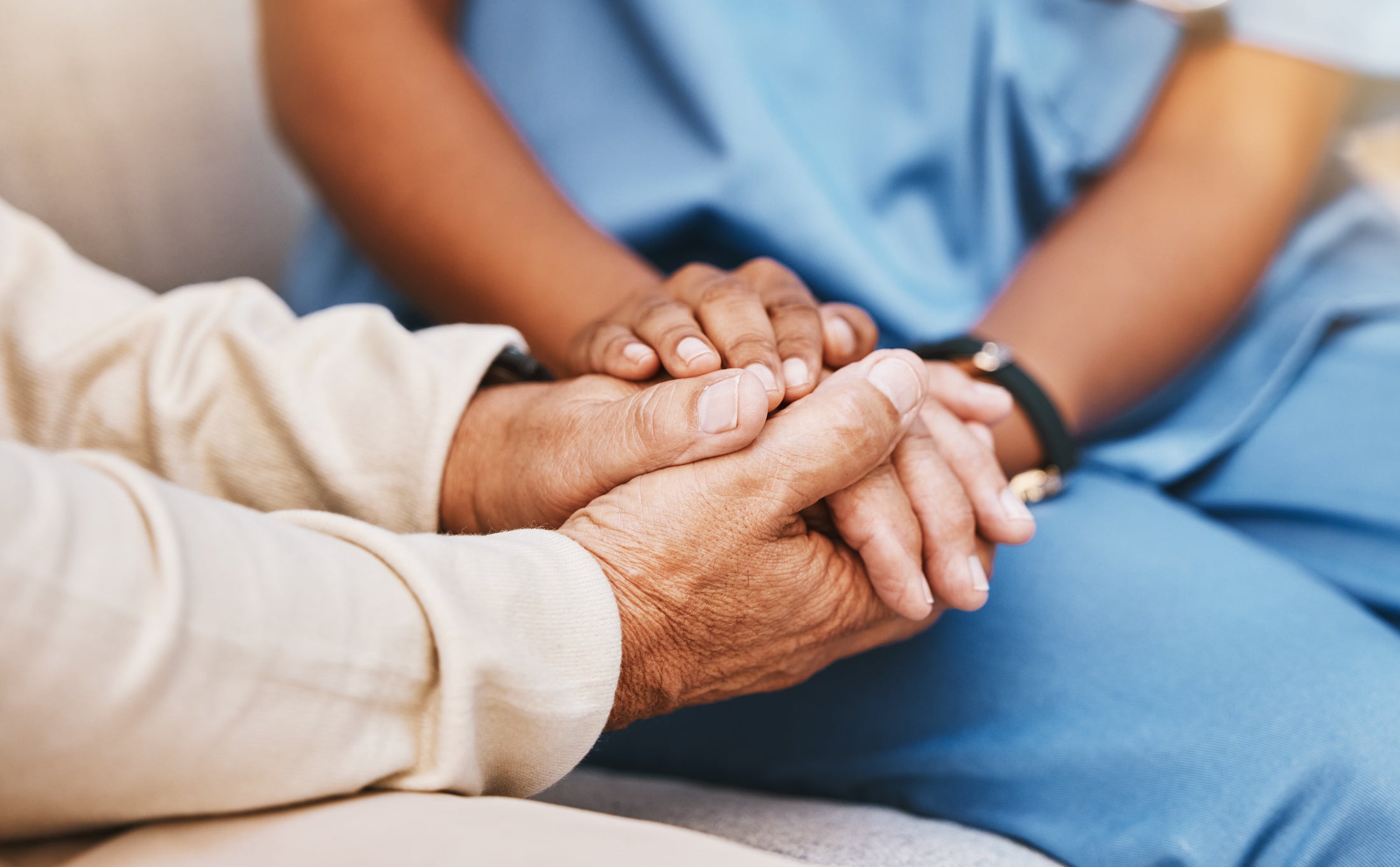 Closeup of hands -- a clinician in blue scrubs holds the hands of a patient