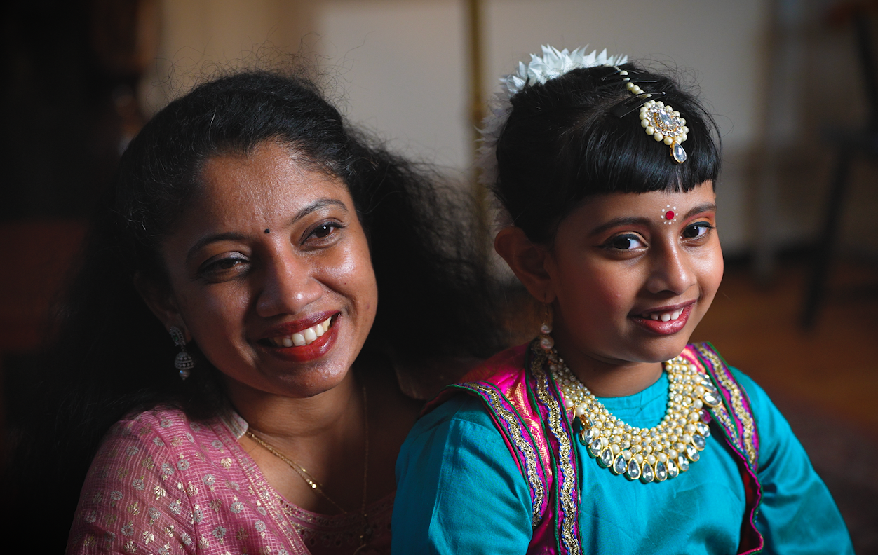 Lakshmi Priya holds her daughter, Mahalakshmi, on her lap. Both are dressed to perform at i-Night in colorful clothing and jewelry.