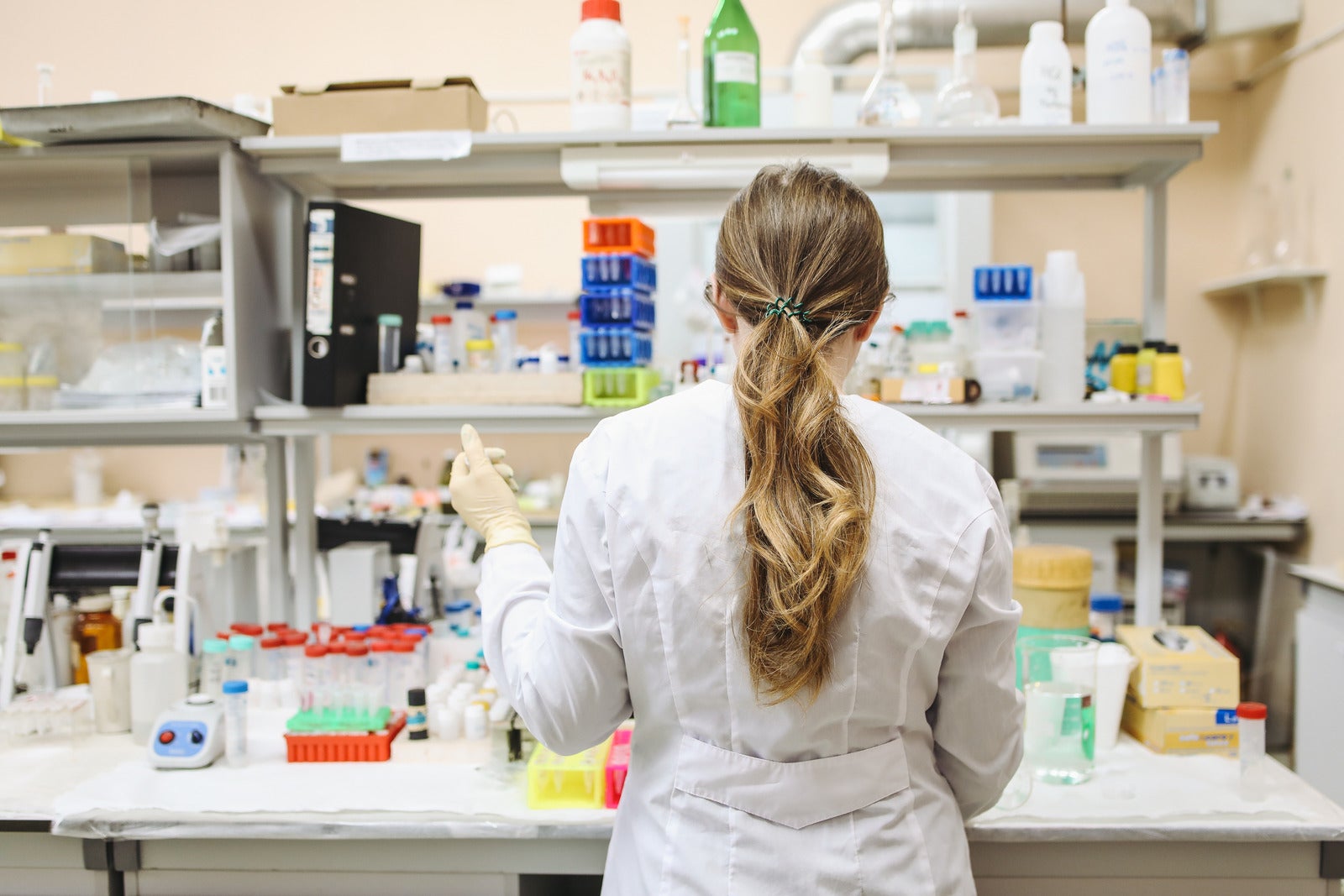 Woman in white long sleeved lab coat standing in a Lab.