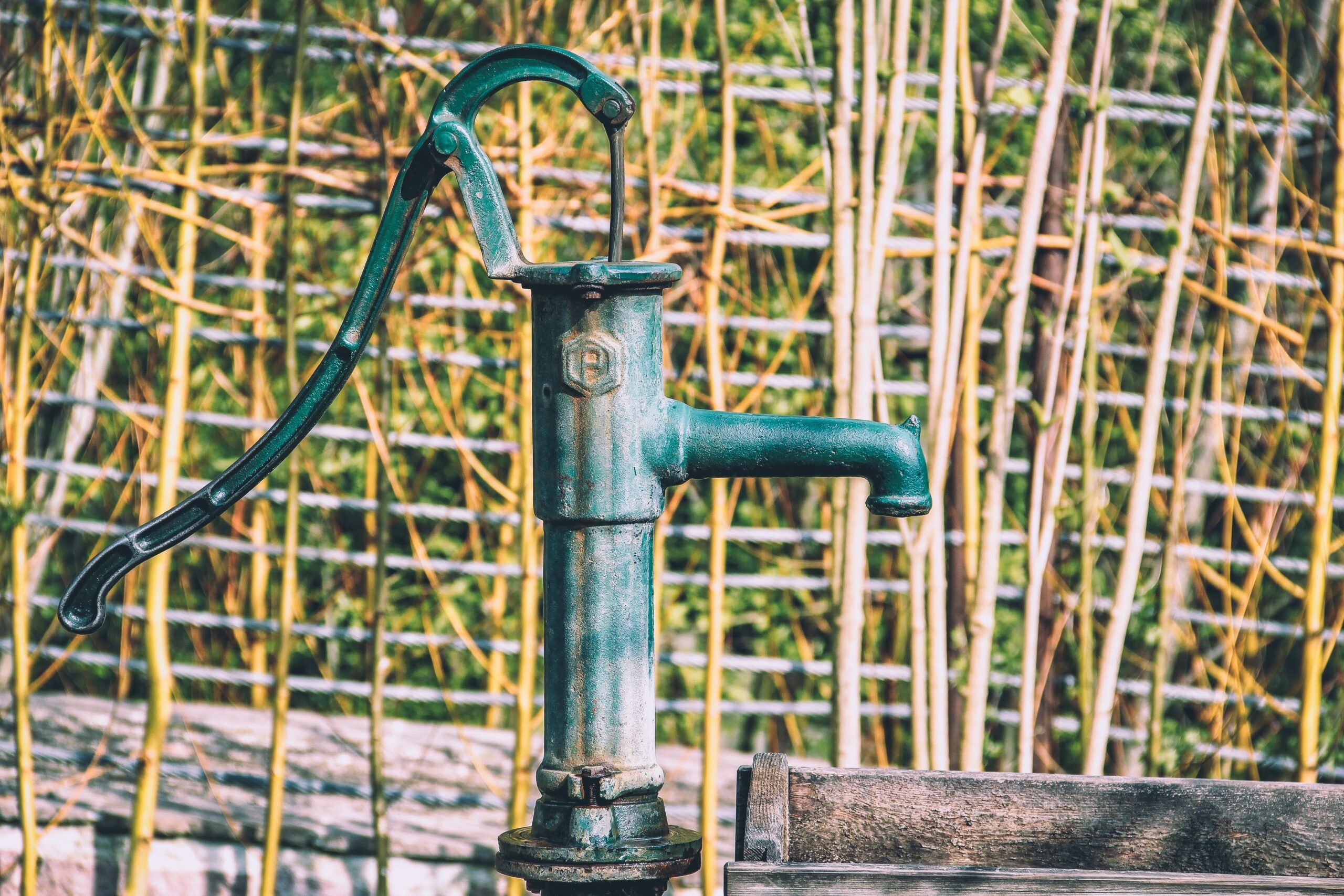 An old-fashioned metal water pump outside over a wooden trough.