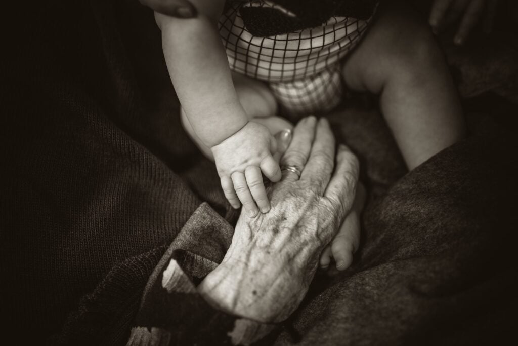 Photo of elderly hands holding a young babies hands.