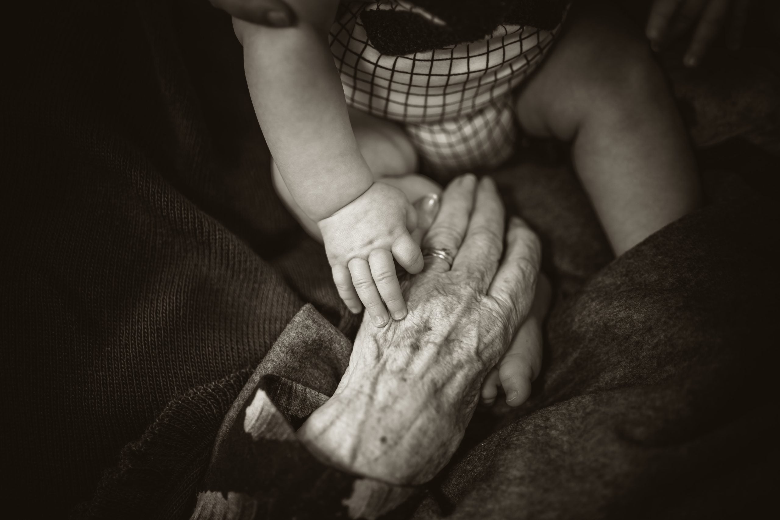 Photo of elderly hands holding a young babies hands.