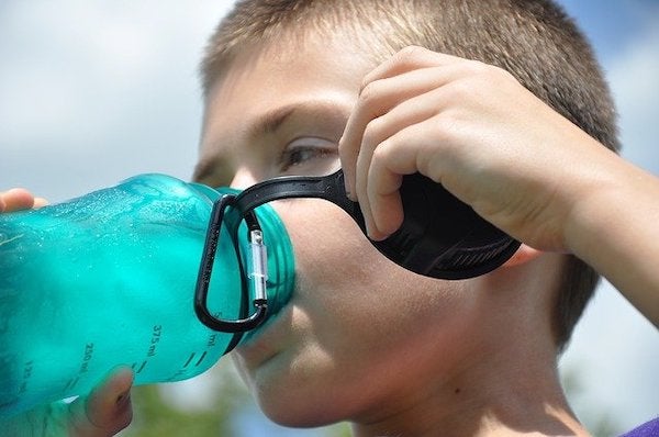 A young boy drinking water out of a reusable plastic water bottle.