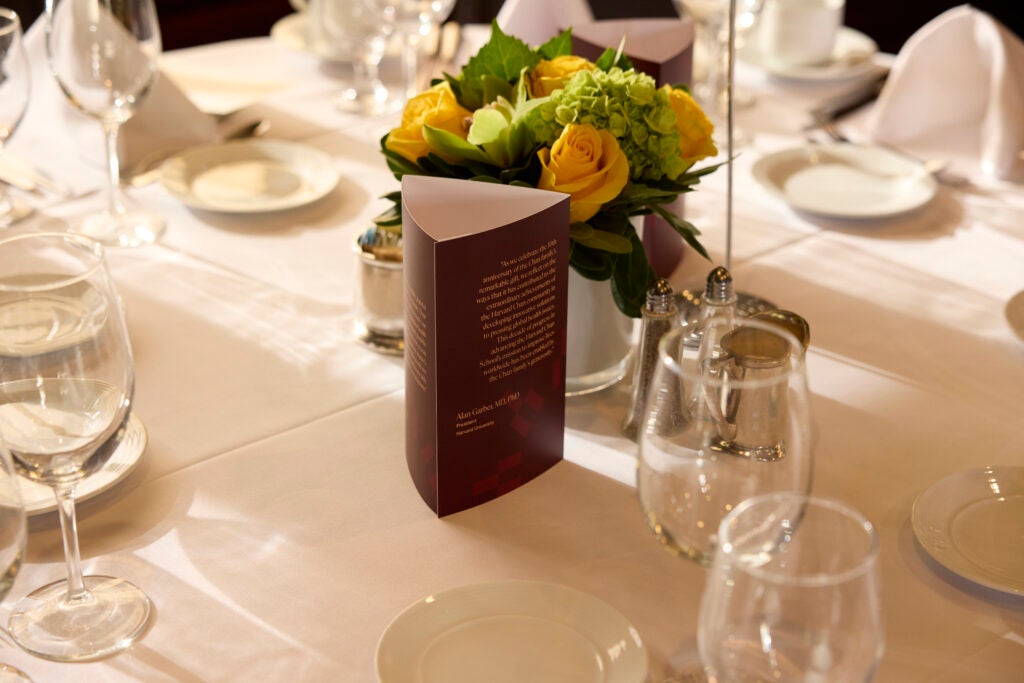 In the center of a table, a crimson trifold stands in front of a floral arrangement of spring greens and yellows. On the trifold is a quote attributed to President Alan Garber. 