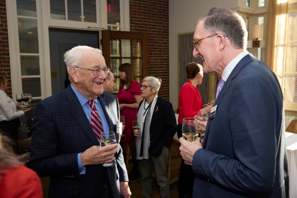 Both standing and holding glasses, Dean Baccarelli laughs with a guest. 