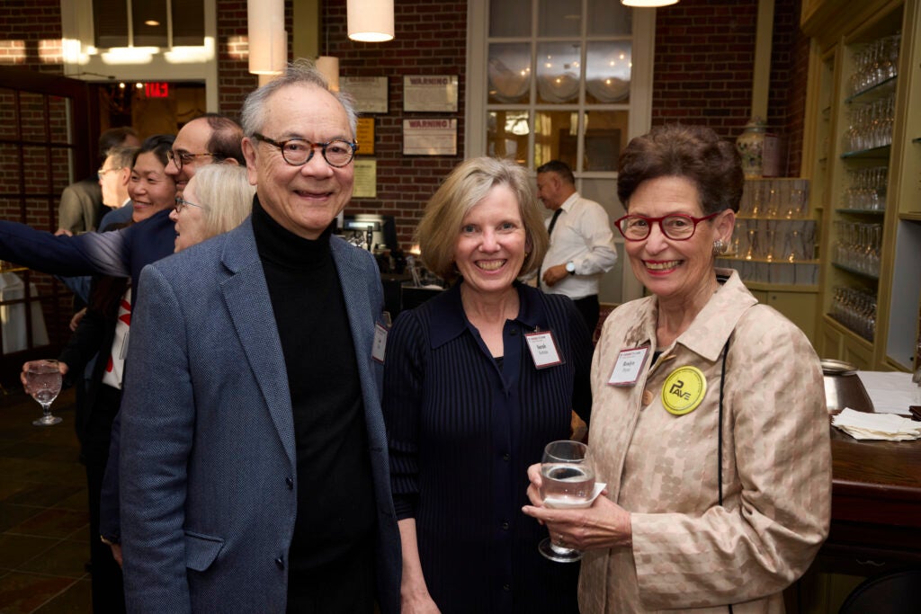 Three guests pose together. The one at right is holding a glass and wears a bright yellow button that says PAVE. 