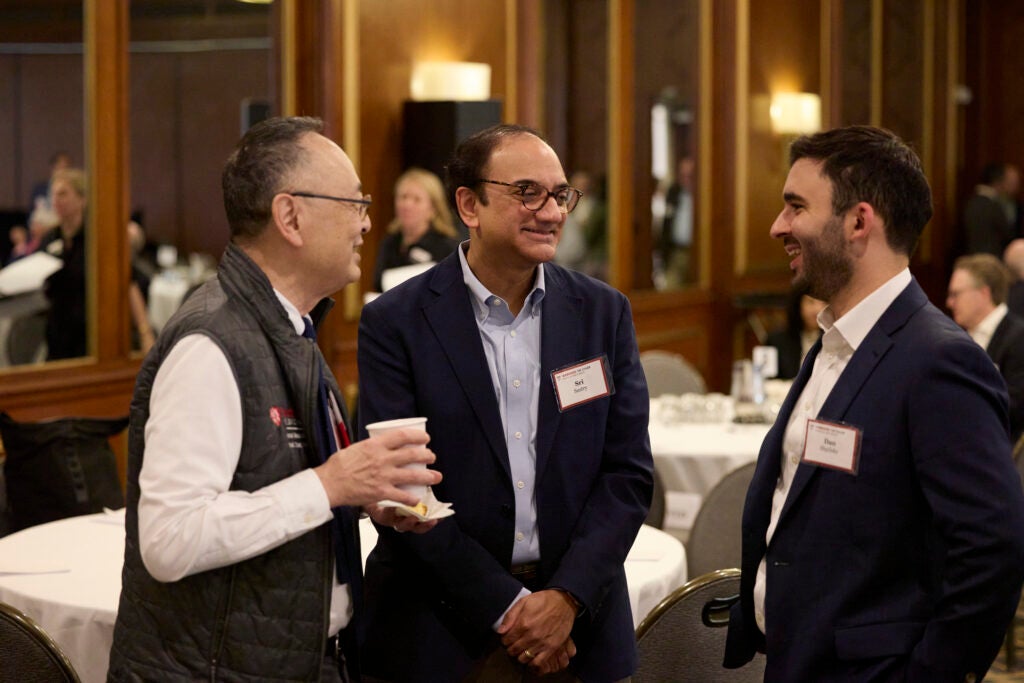 Gerald Chan, holding a cup, chats with two other attendees. 