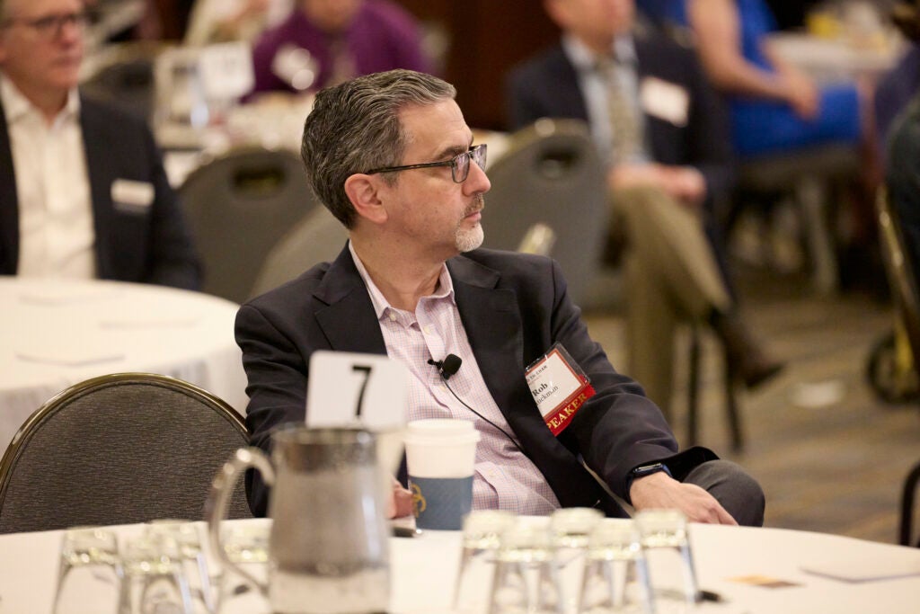 A mean wearing a speaker nametag watches the program from table 7