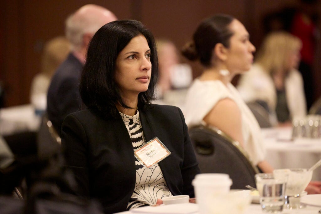 A woman in a dark blazer and graphic blouse focused on the program. 