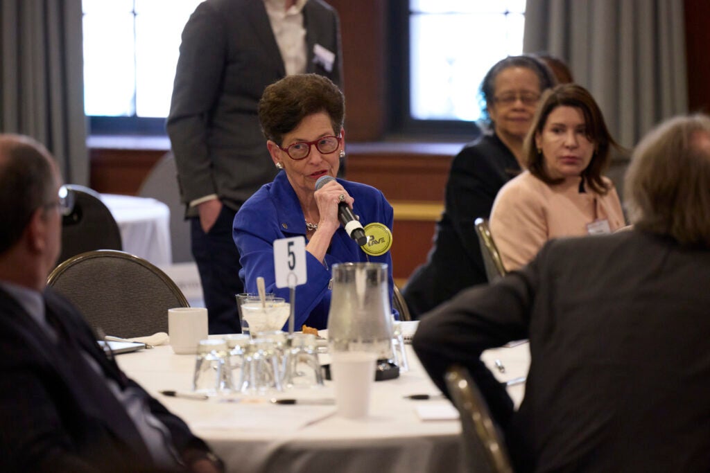 A woman at table five, wearing a bright blue blazer with a yellow button, asks a question.  