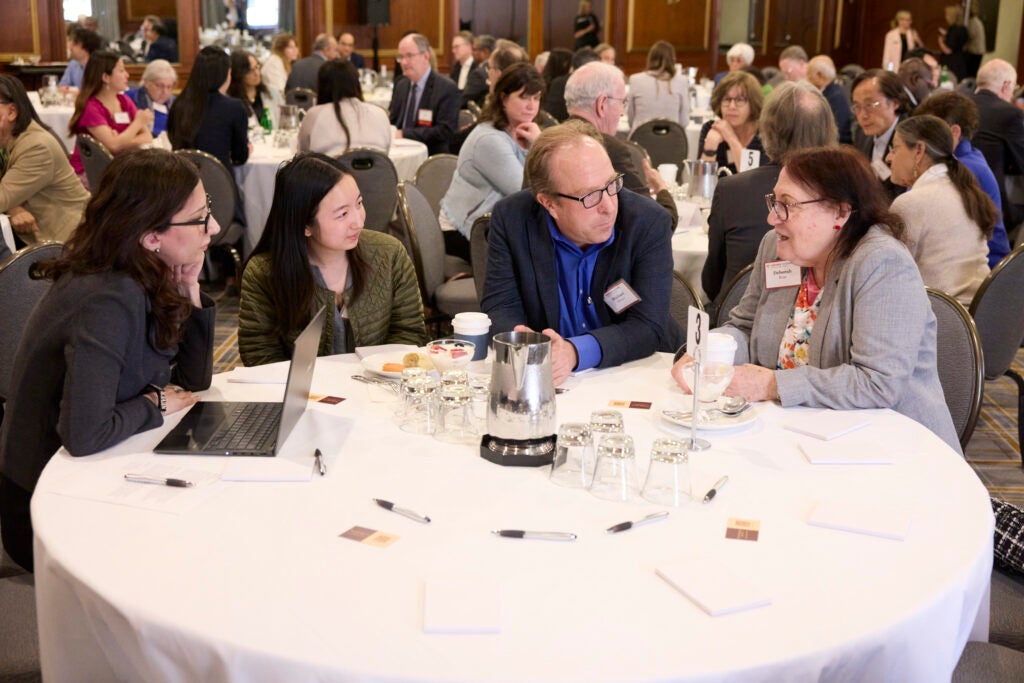Four guests are seated along one side of a round table. The one to the right is speaking ang the others listen. 