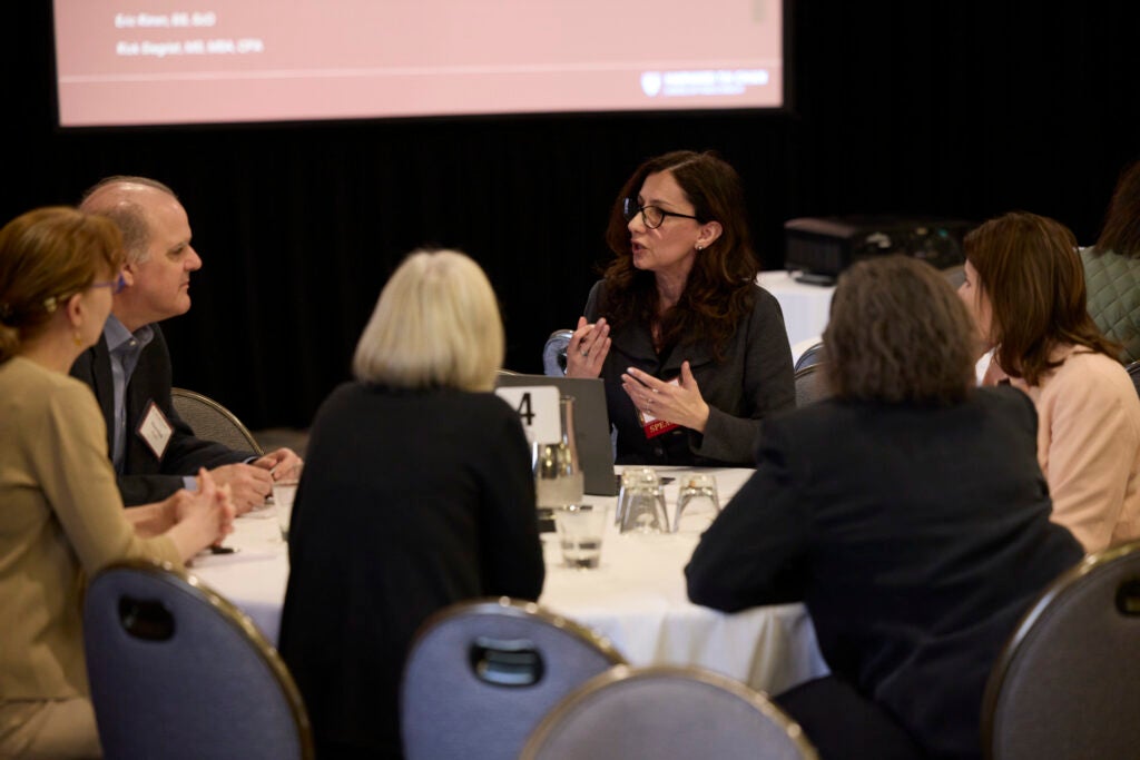 At a full table, a woman gestures while speaking. 