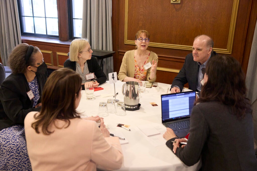 A full table listens attentively asa woman in bright glasses speaks. 