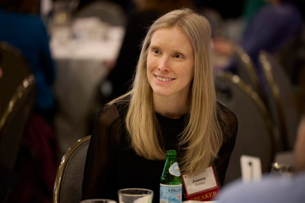 A woman wearing a speaker nametag smiles while listening from her seat. 