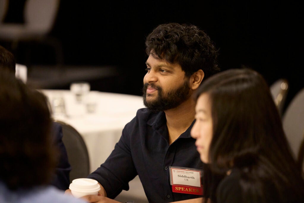 A mean wearing a speaker nametag smiles while listening from his seat
