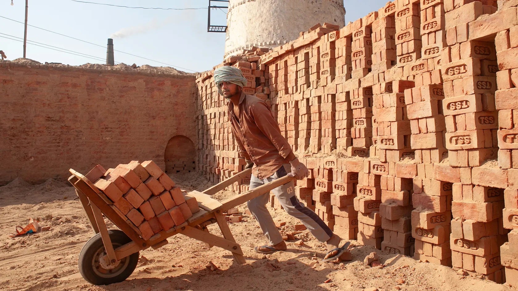 A worker labors in the heat of Uttar Pradesh, India, hauling bricks from a kiln.