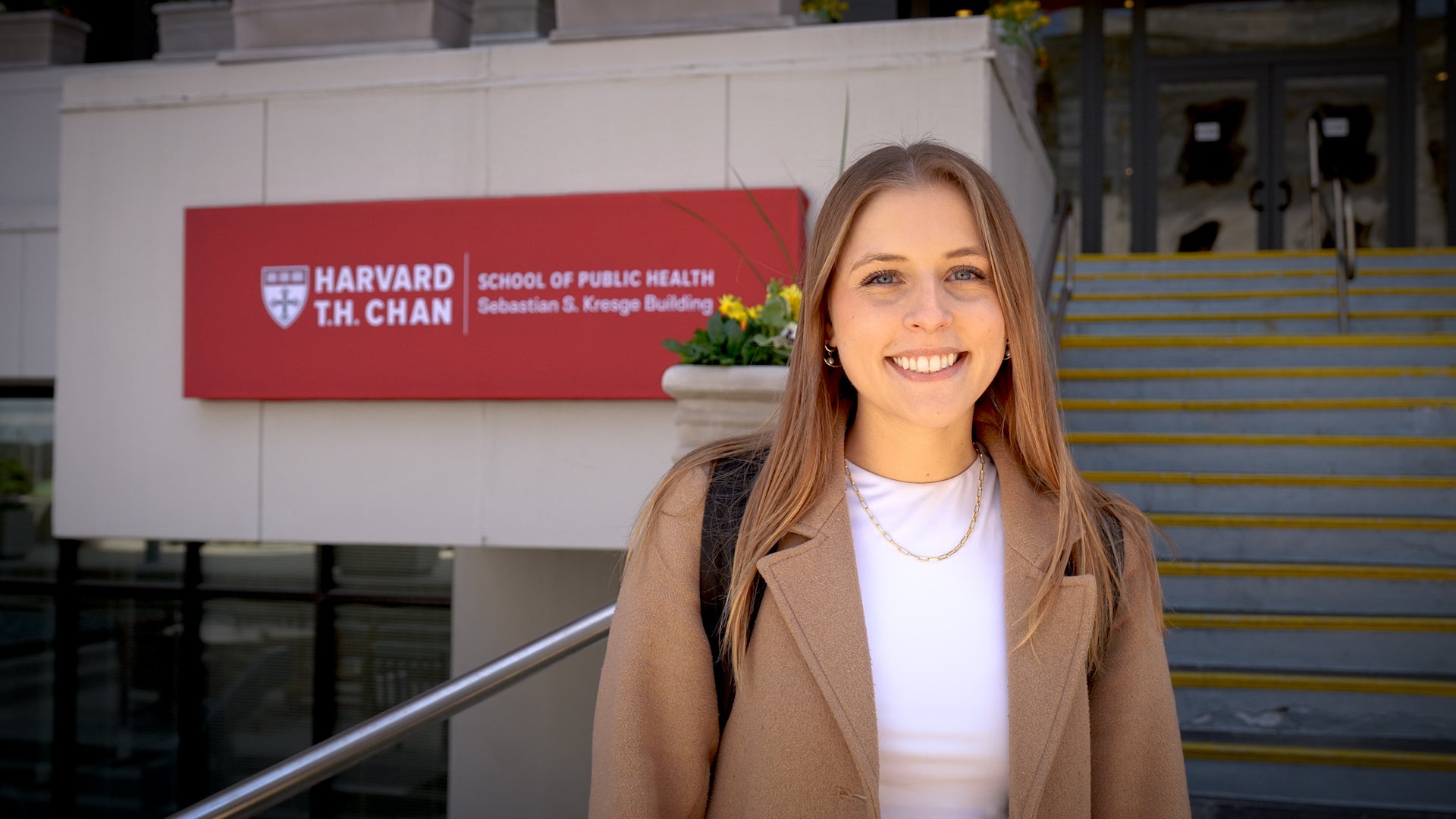 Katie Crum, wearing a white shirt and tan blazer, in front of a sign for the Harvard T.H. Chan School of Public Health