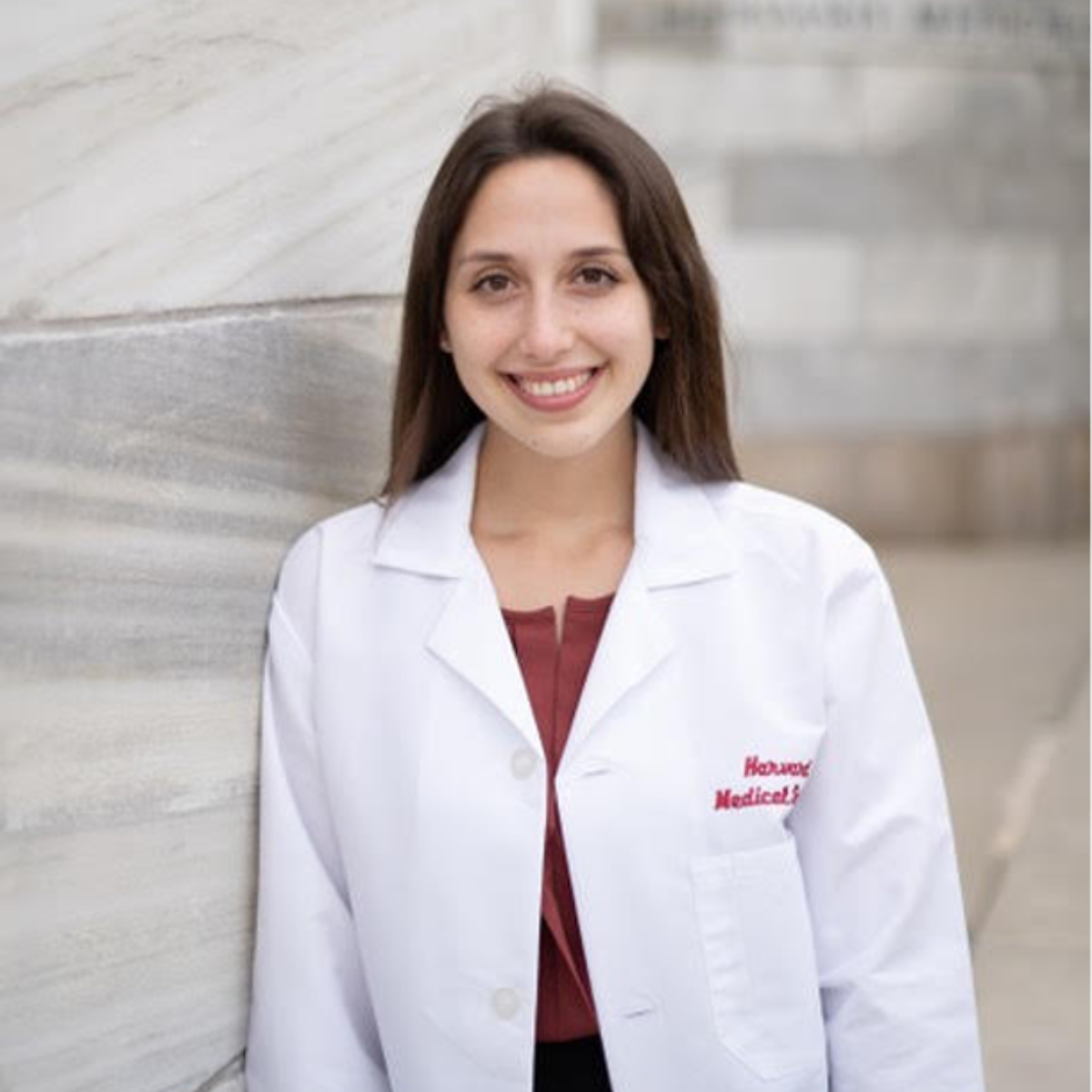 Meddy Kline wearing her lab coat leaning on the white wall of the Harvard medical School