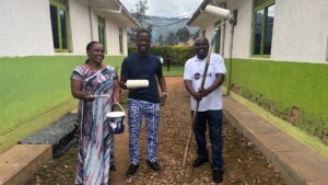 Three people stand outside holding painting supplies.