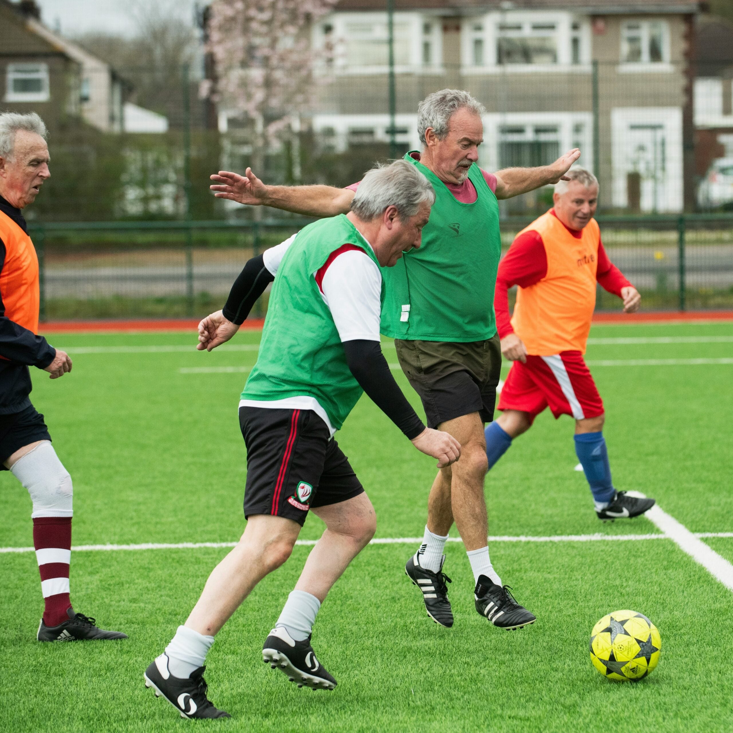 Four older men playing soccer. One man is leaping athletically in the air, attempting to make a pass