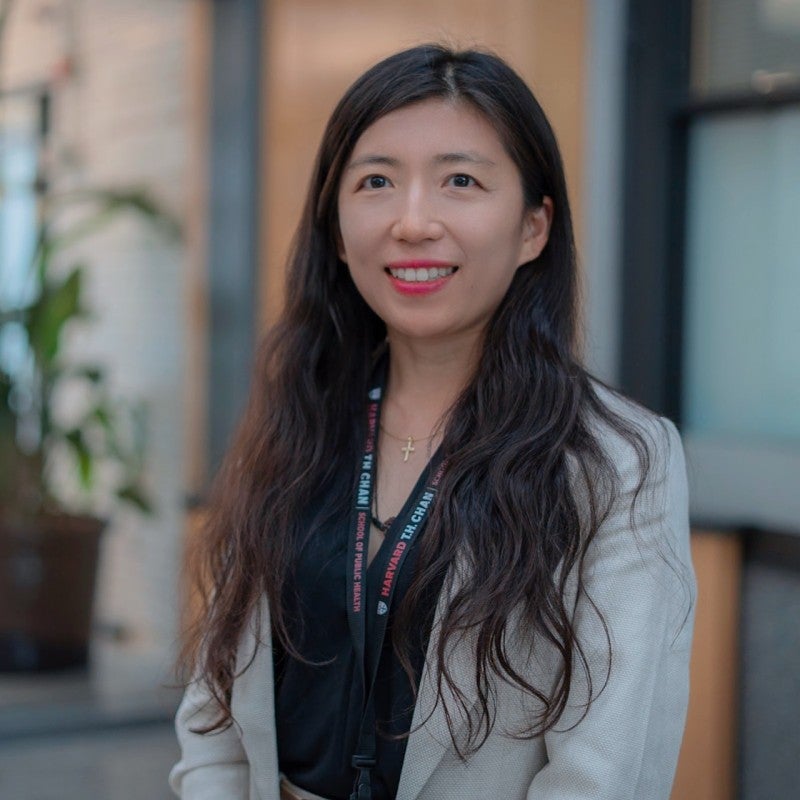 Jie Jane Zhao poses for headshot. She is wearing a tan blazer, a lanyard, and a black top.