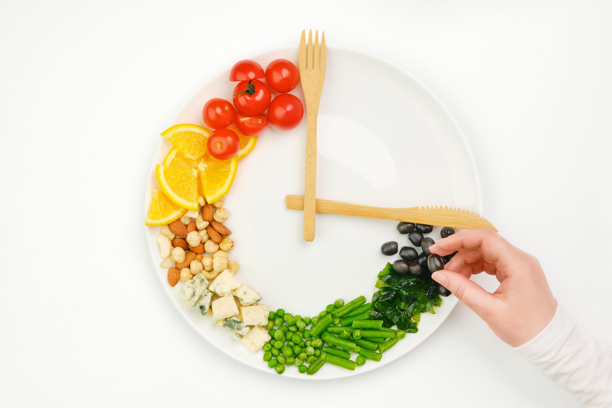 Colorful food and cutlery arranged in the form of a clock on a plate.