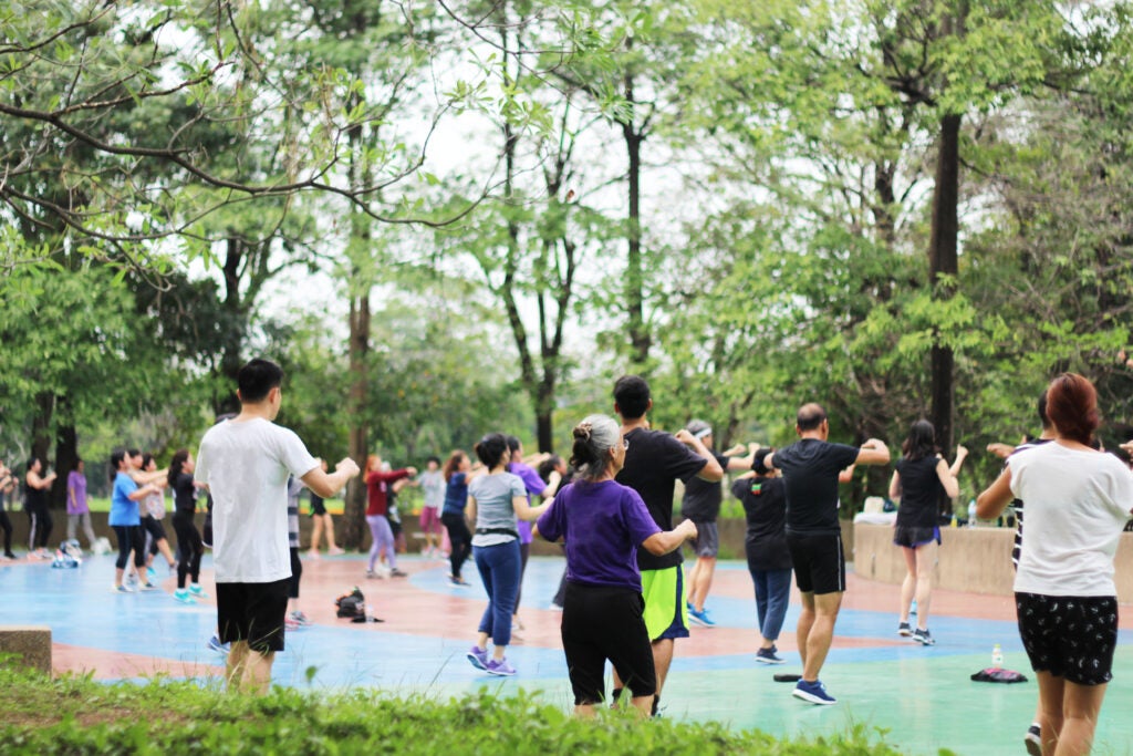 A group of adults of many ages participating in an aerobics class in a public park.