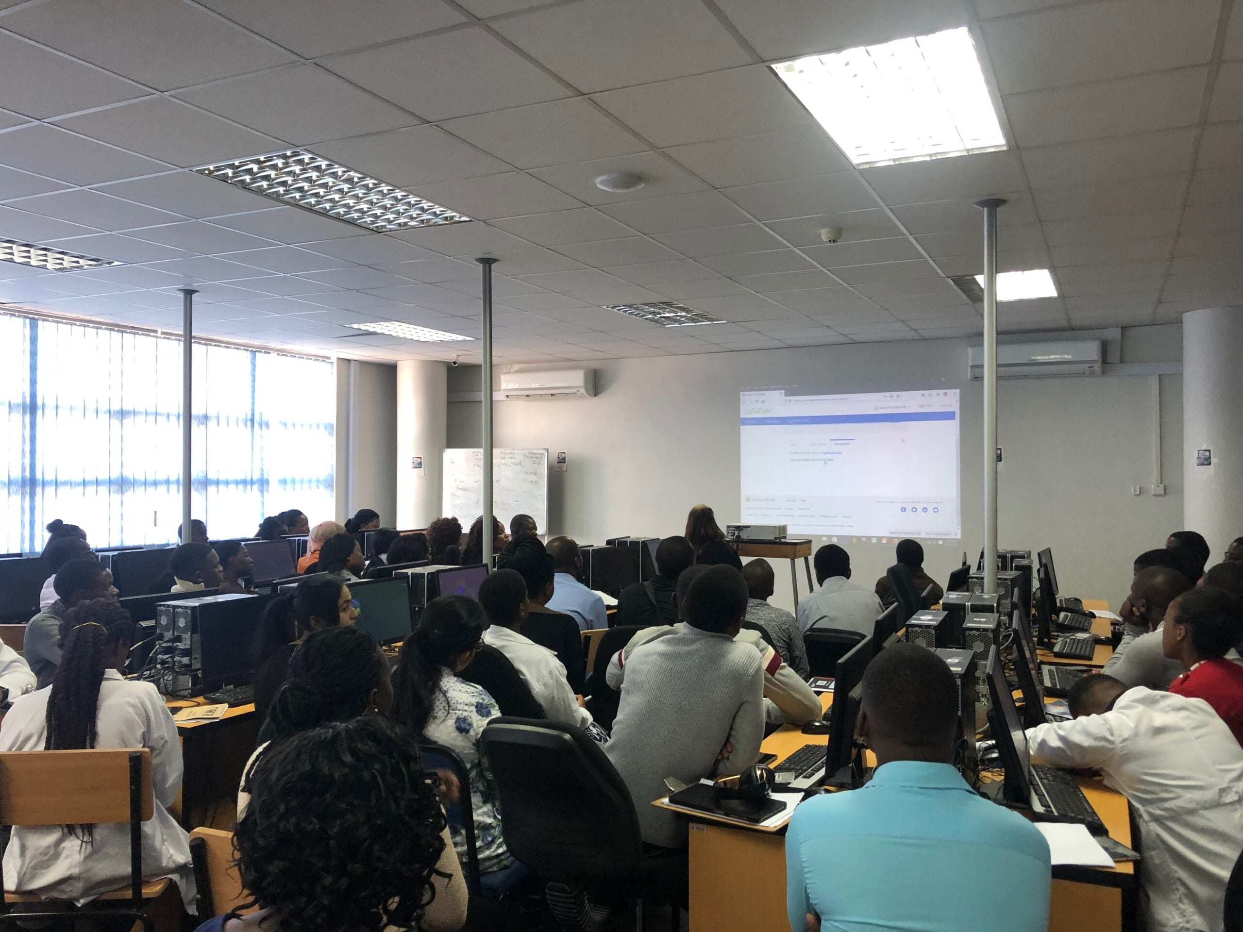Photo of multiple students sitting in a classroom in front of computer screens, looking to front