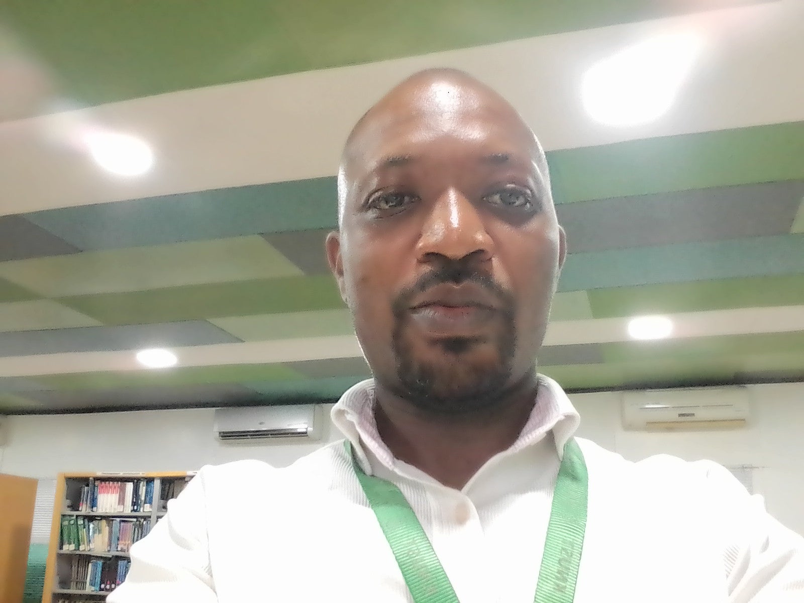 Picture of Yaw Akwoyire with a blue and green background, wearing a white shirt and green lanyard.
