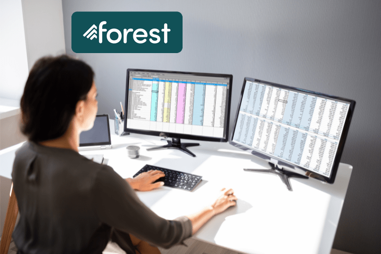 Person at desk looking at two screens with spreadsheets.