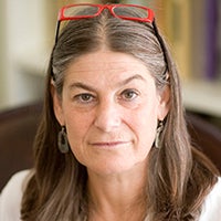 Headshot of a woman with light brown hair and red glasses in her hair with a white shirt
