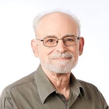 Headshot of a man with white hair and classes wearing a green shirt with an all white background