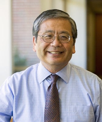 Headshot of a man with gray and black hair and glasses, light purple shirt and tie