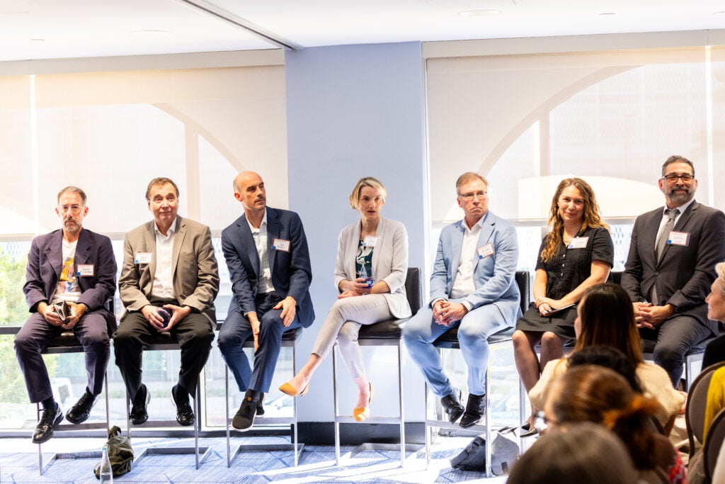 Seven panelists, seated on high chairs in front of windows, at the LA wildfire event. 