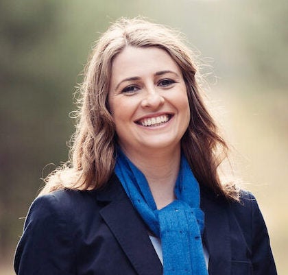 Headshot of woman with dark blonde hair wearing a light blue scarf and dark blue blazer
