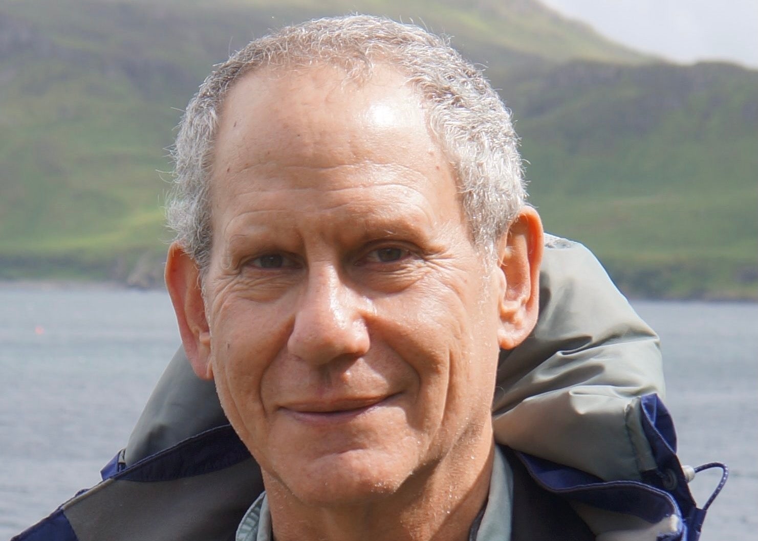 Headshot of a man with gray hair and winter coat with a lake and mountain in the background